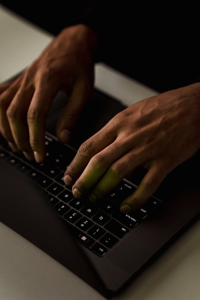 High angle crop anonymous person using netbook and text messaging on keyboard in dark workspace